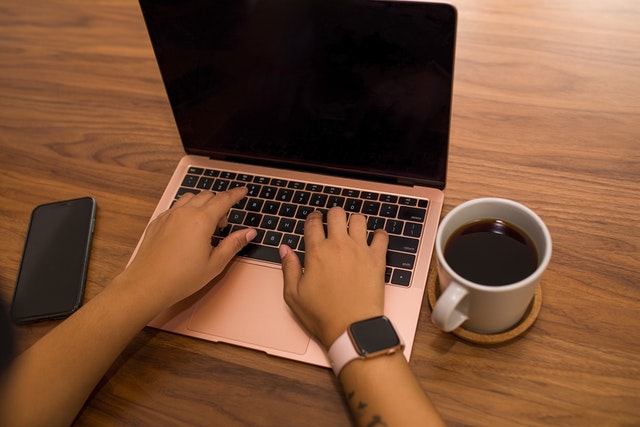 Hands typing on a laptop with a phone and cup of coffee next to it
